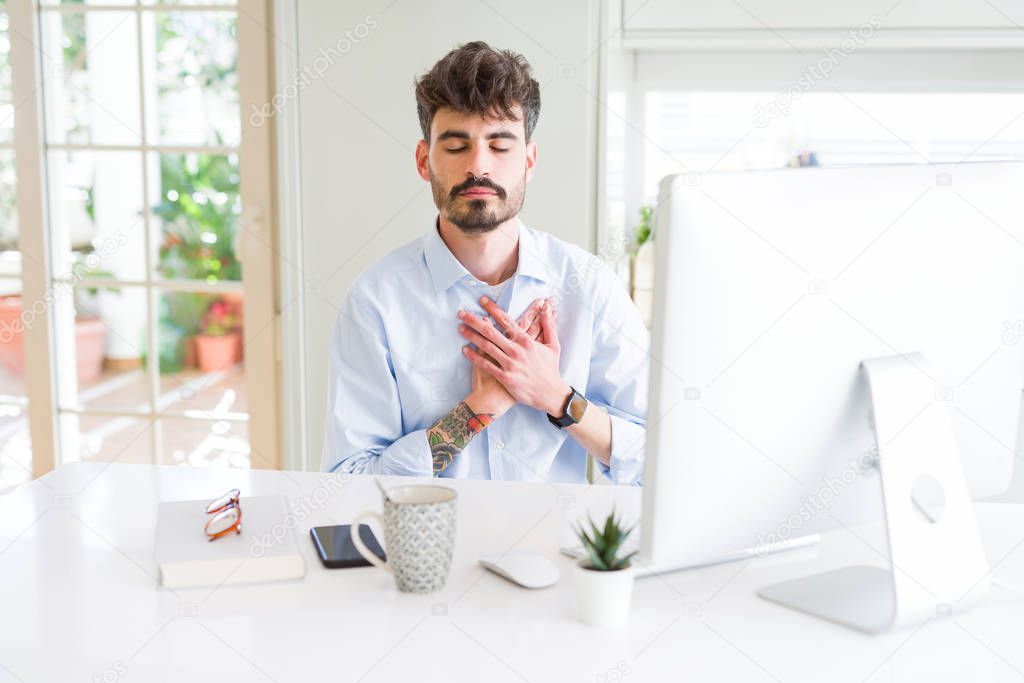 Young business man working using computer smiling with hands on chest with closed eyes and grateful gesture on face. Health concept.