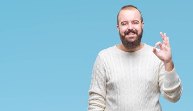 İzole arka plan el ve parmaklar ok işaretiyle yapıyor olumlu gülümseyen üzerinde kış kazak giyen genç beyaz hipster adam. Başarılı ifade.