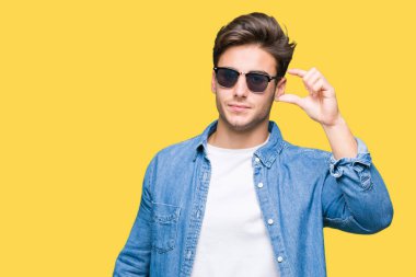 Yakışıklı genç gülümseyen izole arka plan ve süre seyir ve kamera boyutu işaret parmaklarıyla yapıyor el ile kendinden emin eller üzerinde güneş gözlüğü takıyor. Ölçü kavramı.