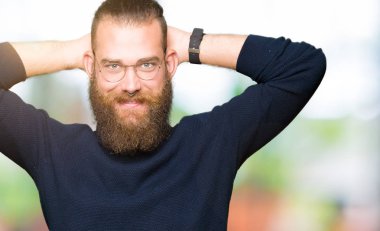 Gözlük ve balıkçı yaka kazak giyen genç sarışın adam rahatlatıcı ve kollar ve eller baş ve boyun, mutlu gülümseyerek arkasında ile germe