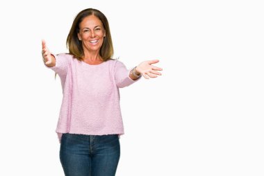 Sarılmak için kollarını açarak gülümseyerek kameraya bakarak izole arka plan üzerinde kış kazak giyen güzel orta yaş yetişkin kadın. Neşeli ifade kucaklayan mutluluk.