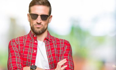 Yüz çapraz kolları olan moda güneş gözlüğü şüpheci ve sinir, onaylamayan ifade giyen yakışıklı adam. Negatif kişi.