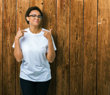 Güzel genç Afro-Amerikan kadın yüzünde gülümseme ile kendinden emin görünüyorsun, kendini gururlu ve mutlu parmakları ile işaret izole arka plan üzerinde gözlük.