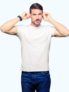 Casual beyaz t-shirt kapsayan kulakları parmakları ile yüksek sesle müzik gürültü rahatsız ifade ile giyen yakışıklı adam. Sağır kavramı.