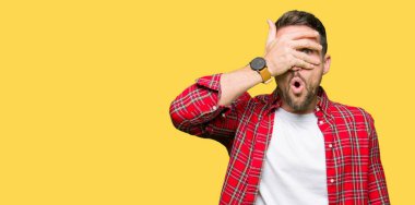 Yakışıklı adam rahat gömlek yüz ve gözler el ile kapsayan şok bakmak giyen mahcup ifadeyle parmaklarımın arasından bakan.