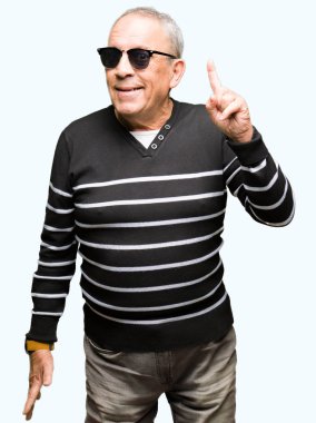 Yakışıklı kıdemli dostum giyen kış kazak ve güneş gözlüğü ile başarılı fikir parmak işaret. Çıktıktan ve mutlu. Bir numara.