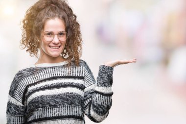 Güzel esmer kıvırcık saçlı Genç kız neşeli sunulması ve kameraya bakarak avucunun ile işaret gülümseyen izole arka plan üzerinde gözlük.
