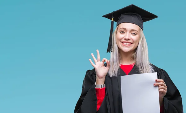 優秀なシンボルの指で サインをして孤立の背景上の学位を保持する大学院の制服を着て若いブロンドの女性 — ストック写真