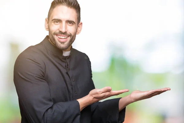 Young Christian priest over isolated background Pointing to the side with hand and open palm, presenting ad smiling happy and confident