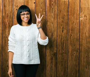 Güzel genç Afro-Amerikan kadın gözlük gösterilen ve parmakları ile işaret izole arka plan üzerinde ise kendinden emin ve mutlu gülümseyerek üçüncüsü.