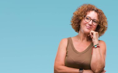 Orta yaş İspanyol kadın gözlük ile izole arka plan üzerinde çene düşünme hakkında soru, dalgın ifade ver. Düşünceli yüzüyle gülümsüyor. Şüphe kavramı.