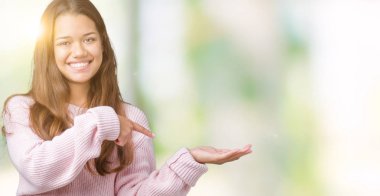 Hayret ve el ile sunulması ve parmak ile işaret ederken kameraya gülümseyen izole arka plan üzerinde pembe kış kazak giyen genç güzel esmer kadın.