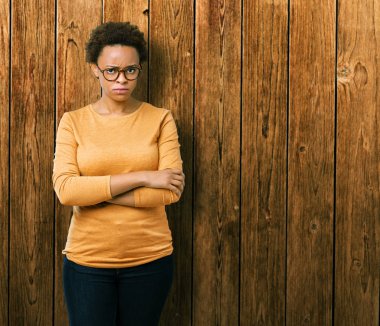 İzole arka plan şüpheci ve çapraz kolları olan yüzündeki gergin, onaylamayan ifade gözlüklü genç güzel Afrikalı-Amerikalı kadın. Negatif kişi.