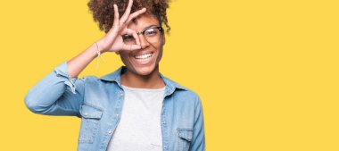 Güzel genç Afro-Amerikan kadın gülümsüyor, parmakları ile mutlu yüz üzerinden seyir göz el ile ok jest yapıyor izole arka plan üzerinde gözlük.