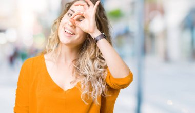 Güzel genç sarışın kadın gülümsüyor, parmakları ile mutlu yüz üzerinden seyir göz el ile ok jest yapıyor izole arka plan üzerinde.