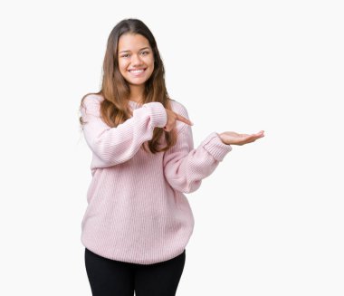 Hayret ve el ile sunulması ve parmak ile işaret ederken kameraya gülümseyen izole arka plan üzerinde pembe kış kazak giyen genç güzel esmer kadın.