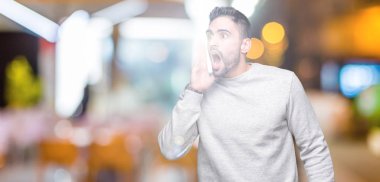 Bağırarak ve ağzı üzerinde el ile yan için çığlık izole arka plan üzerinde kazak giyen genç yakışıklı adam. İletişim kavramı.