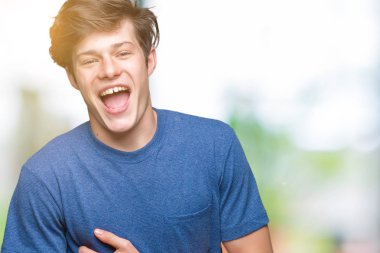 Mavi t-shirt üzerinde izole giyen genç yakışıklı adam arka plan gülen ve komik deli şaka çünkü yüksek sesle zor gülüyor. Mutlu ifade.
