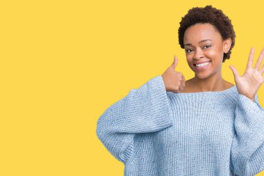 Gösterilen ve parmakları ile işaret izole arka plan üzerinde bir kazak giyen genç güzel Afrikalı-Amerikalı kadın kendinden emin ve mutlu gülümseyerek süre 6 numara.