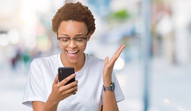 Smartphone üzerinde kocaman bir gülümseme ile çığlık zaferini kutluyor ve ellerini kaldırdı izole arka plan çok mutlu ve heyecanlı, kazanan ifade kullanan genç Afro-Amerikan kadın