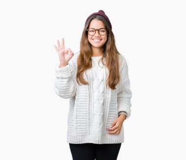 Gözlük ve kış şapka gülümseyen izole arka plan üzerinde el ve parmaklar ok işaretiyle yapıyor olumlu giyen genç güzel esmer hipster kadın. Başarılı ifade.