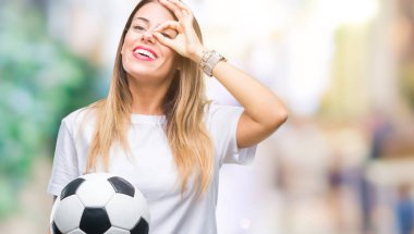 Futbol topu ile mutlu yüz el parmaklarının arasından seyir göz üzerinde ok işaretiyle yapıyor gülümseyen izole arka plan üzerinde tutan genç güzel kadın