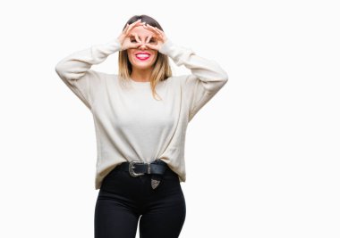 Genç güzel kadın dilini, parmaklarının arasından baktığını yapışmasını dürbün gibi ok jest yapıyor izole arka plan üzerinde rahat beyaz kazak. Deli ifade.