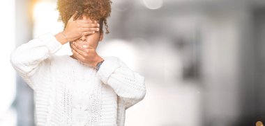 İzole arka plan kaplaması gözler ve ağız el ile üzerinden kış kazak giyen güzel genç Afro-Amerikan kadın şaşırttı ve şok. Duygu gizleme