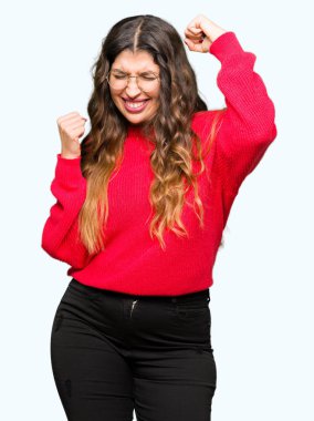 Gülümseyen ve başarı için çığlık çok mutlu ve heyecanlı kaldırdı, silah ile kazanan jest yapıyor kırmızı gözlük takan genç güzel kadın. Kutlama kavramı.