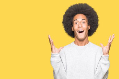 Afrikalı-Amerikalı genç afro saçlı deli ve çığlık kaldırdı ve açık gözleri heyecanlı silah ile başarı için hayran sportif kazak kutluyor giyiyor. Kazanan kavramı