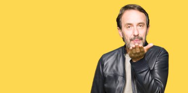 Orta yaş yakışıklı adam siyah deri ceketli bir öpücük el ile güzel ve seksi olmak hava üfleme kamera bakıyor. Aşk ifade.