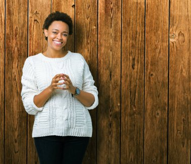 Arka plan eller üzerinde kazak giyen güzel genç Afro-Amerikan kadın birlikte izole ve rahat ve neşeli gülümseyen parmak çarpı işareti. Başarı ve iyimser