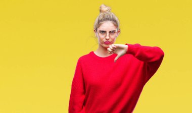 Mutsuz ve kızgın ret gösterilen ve başparmak aşağı hareketi ile negatif seyir izole arka plan üzerinde kırmızı kazak ve gözlük giyen genç güzel sarışın kadın. Kötü ifade.