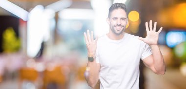 Gösterilen ve parmakları ile işaret izole arka plan üzerinde rahat beyaz t-shirt giyen genç adam numara 9 kendinden emin ve mutlu gülümseyerek süre.