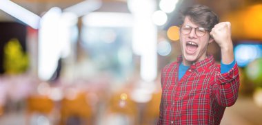 Üzerinde gözlük takan genç yakışıklı adam arka plan kızgın izole ve kızgın yetiştirme hayal kırıklığı ve öfke ile bağırarak süre öfkeli yumruk. Öfke ve agresif kavramı.