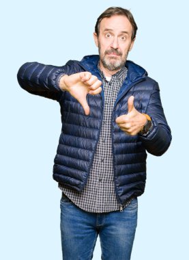 Yukarı ve aşağı yapıyor başparmak kış ceket giyen orta yaş yakışıklı adam, anlaşmazlık ve anlaşma ifade. Deli çatışma