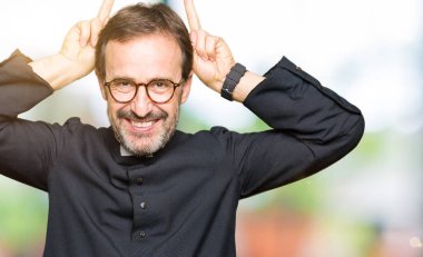 Katolik giyen orta yaş rahip adam robe komik poz ve baş parmak ile deli tavşan kulakları neşeli gülümseyen