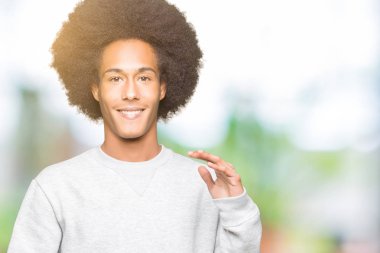 Afrikalı-Amerikalı genç afro saçlı sportif kazak ile büyük ve büyük boy işaret, ölçü birimi sembol gösteren el eller giyiyor. Kameraya bakarak gülümsüyordu. Ölçüm kavramı.