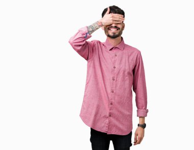 Gülümsüyor ve gözleri için sürpriz kapsayan yüz el ile gülüyor izole arka plan üzerinde pembe gömlek giymiş yakışıklı delikanlı. Kör kavramı.