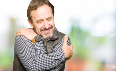 Orta yaş yakışıklı adam kendini mutlu ve olumlu sarılma, kendinden emin gülümseyen kış yelek giyiyor. Kendi aşk ve öz bakım