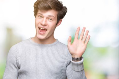 Yakışıklı delikanlı izole arka plan Waiving mutlu selam söyleyerek üzerinde kış kazak ve gülümseyen, dostça karşılama jest