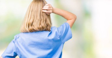 İzole arka plan geriye düşünme hakkında şüphe ile baş taraftan üzerinde tıbbi üniforma giyen güzel genç doktor kadın