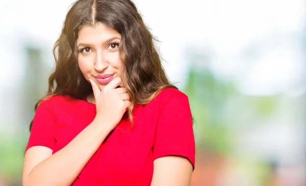 Young beautiful woman wearing casual t-shirt looking confident at the camera with smile with crossed arms and hand raised on chin. Thinking positive.