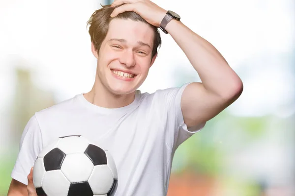 サッカー サッカー ボールの頭の上の手を強調した分離の背景の上に保持している若い男が恥と驚きの顔でショックを受けて怒っているとイライラします 恐怖と動揺の間違い — ストック写真