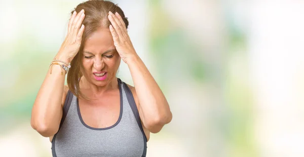 Beautiful middle age woman wearing sport clothes over isolated background suffering from headache desperate and stressed because pain and migraine. Hands on head.