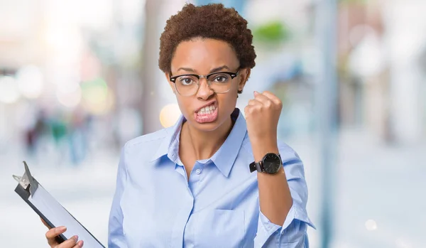 Young african american businesss woman holding clipboard over isolated background annoyed and frustrated shouting with anger, crazy and yelling with raised hand, anger concept