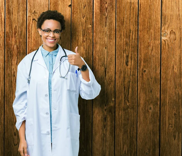 年轻的非洲女医生在孤立的背景下穿着医疗外套做快乐的大拇指与手的手势 查看显示成功的相机的审批表情 — 图库照片