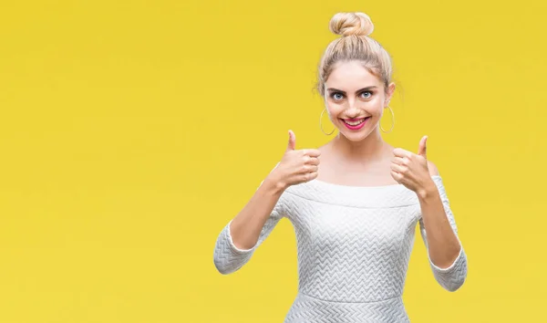 Young beautiful blonde and blue eyes woman over isolated background success sign doing positive gesture with hand, thumbs up smiling and happy. Looking at the camera with cheerful expression, winner gesture.