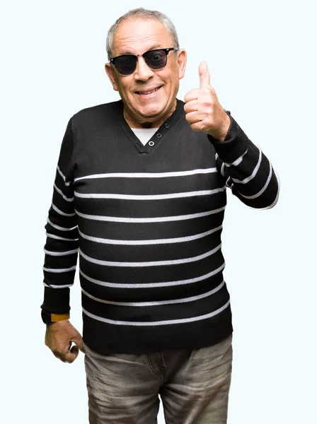 英俊的老人穿着冬天的毛衣和太阳镜做快乐的大拇指用手的手势 通过显示成功来批准镜头的表达 — 图库照片