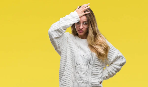 Young beautiful blonde woman wearing winter sweater and sunglasses over isolated background surprised with hand on head for mistake, remember error. Forgot, bad memory concept.